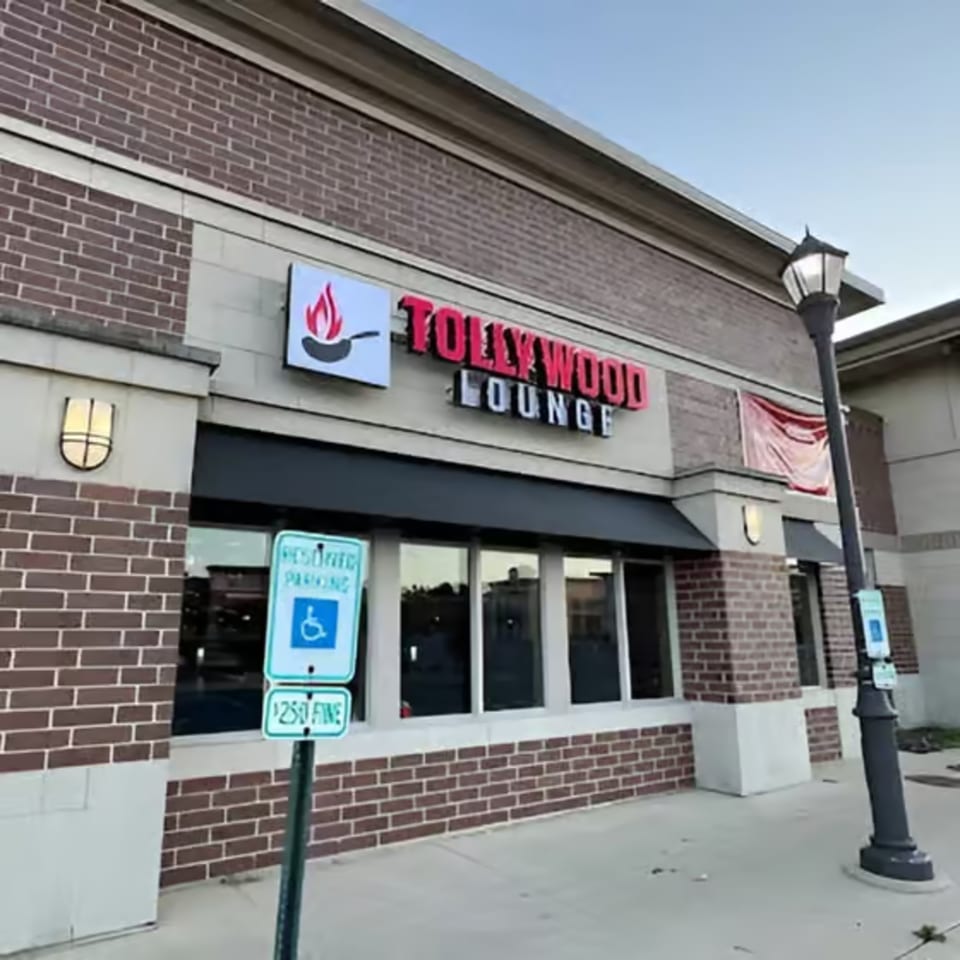 Exterior of Tollywood Lounge, a brick building with a black awning and red sign, under a clear sky.