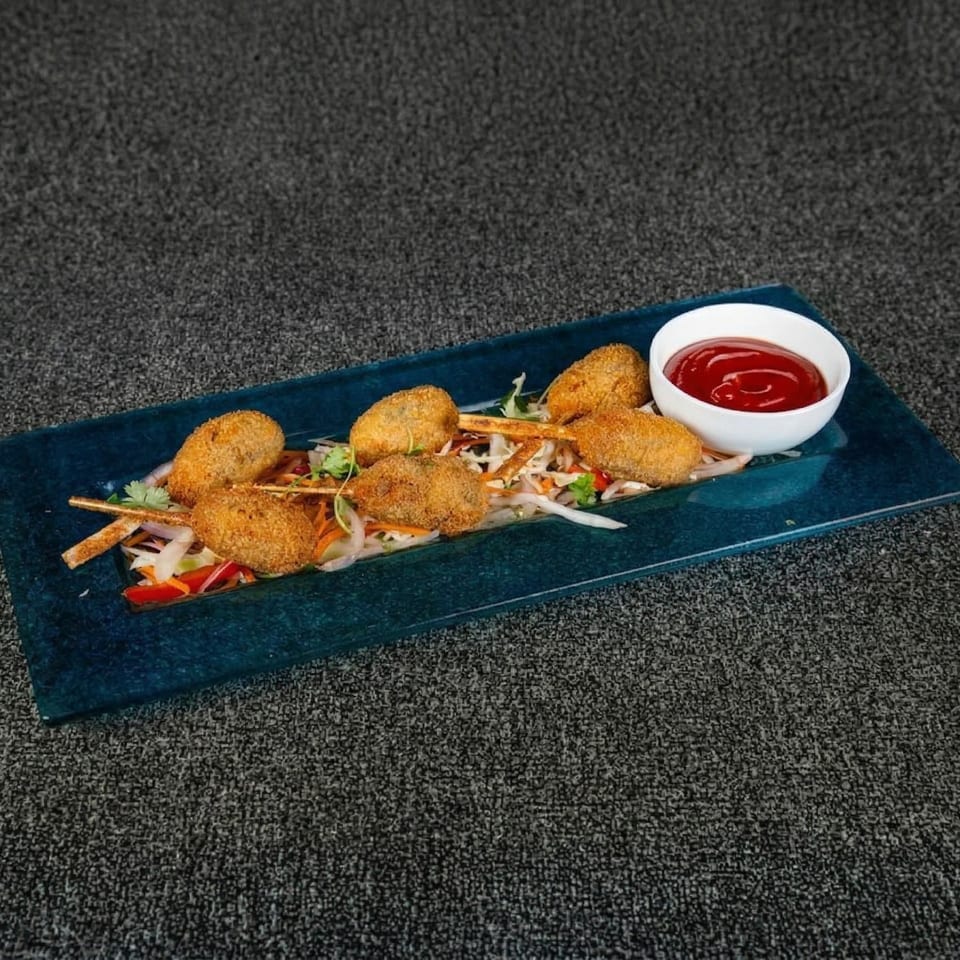 Breaded fried food on skewers with shredded vegetables and a side of ketchup on a blue plate.