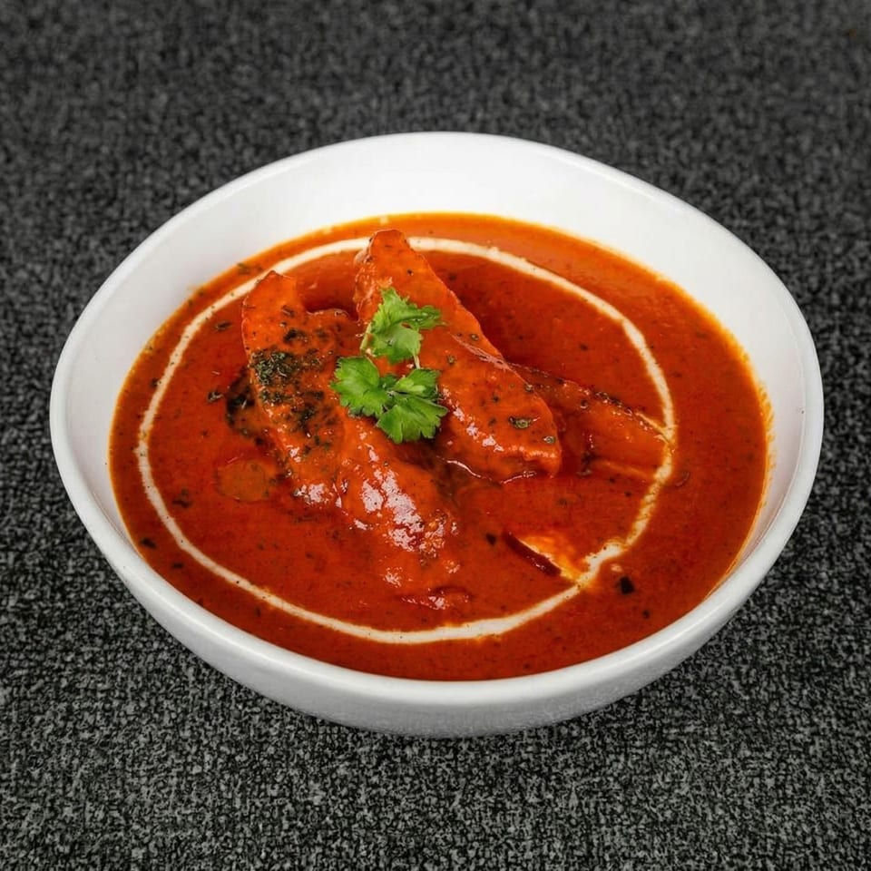 Chicken tikka masala in a white bowl, garnished with cream swirls and fresh cilantro.
