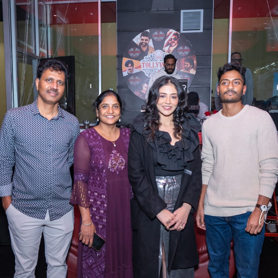 Four people, two men and two women, pose for a photo in front of a Tollywood poster.
