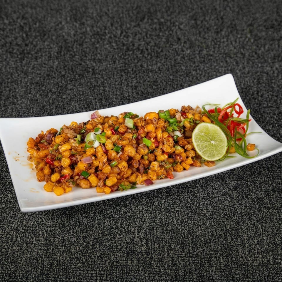 Sweet corn kernels mixed with spices, onions, and peppers, garnished with a lime slice and greens.