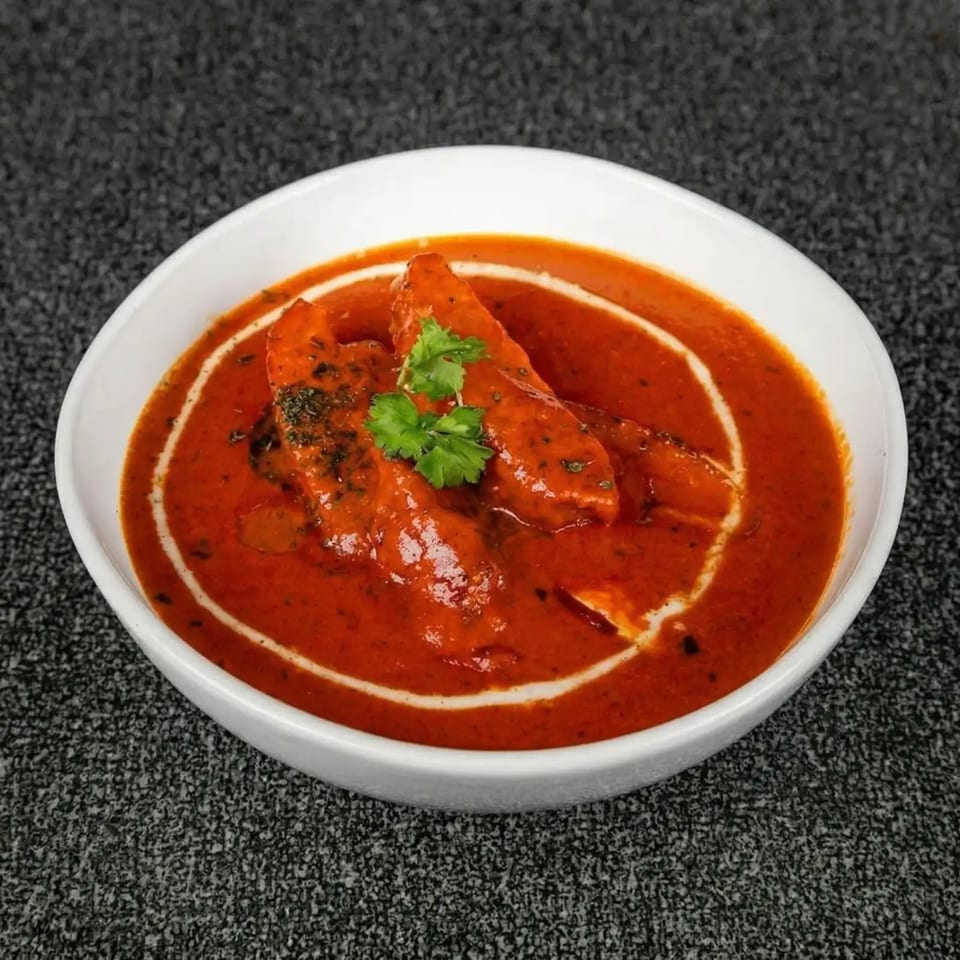Chicken tikka masala in a white bowl, garnished with cream swirls and fresh cilantro.