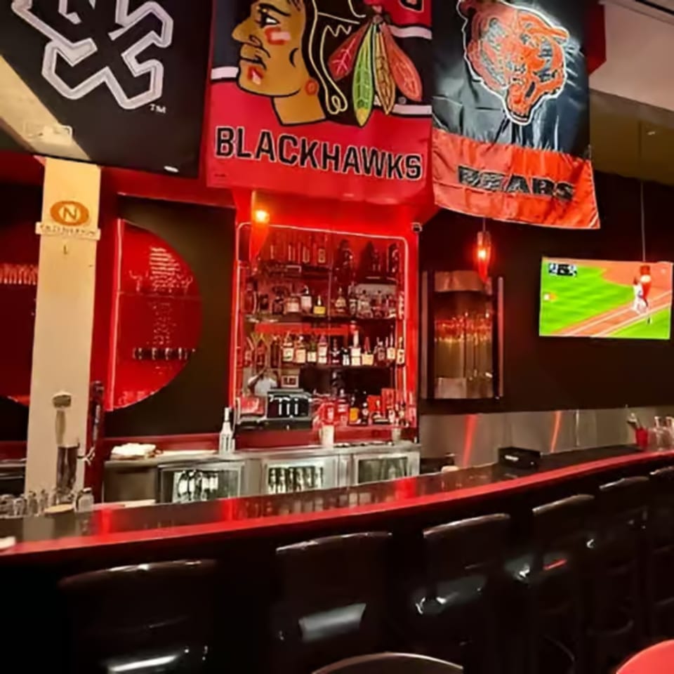 A sports bar with Chicago team flags, a well-stocked bar, and a baseball game on TV.