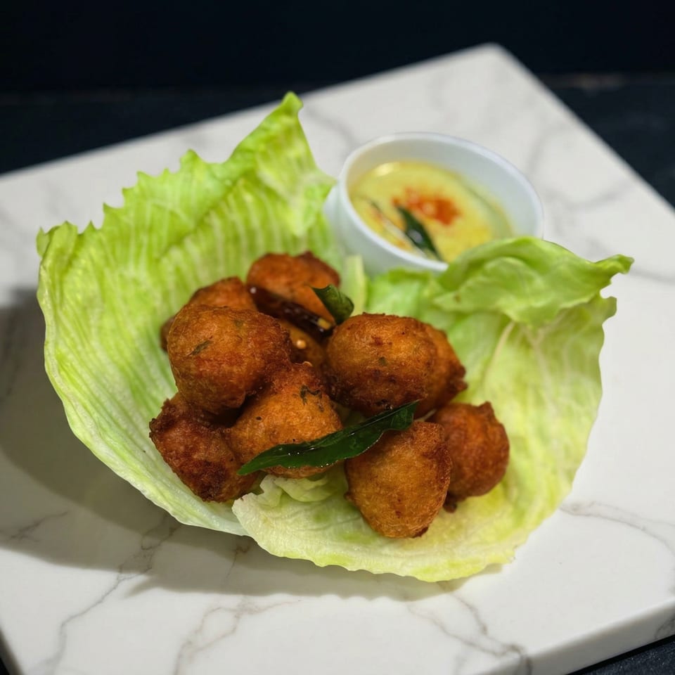 Golden-brown fried fritters served in a vibrant green lettuce cup with a side of yellow dipping sauce.