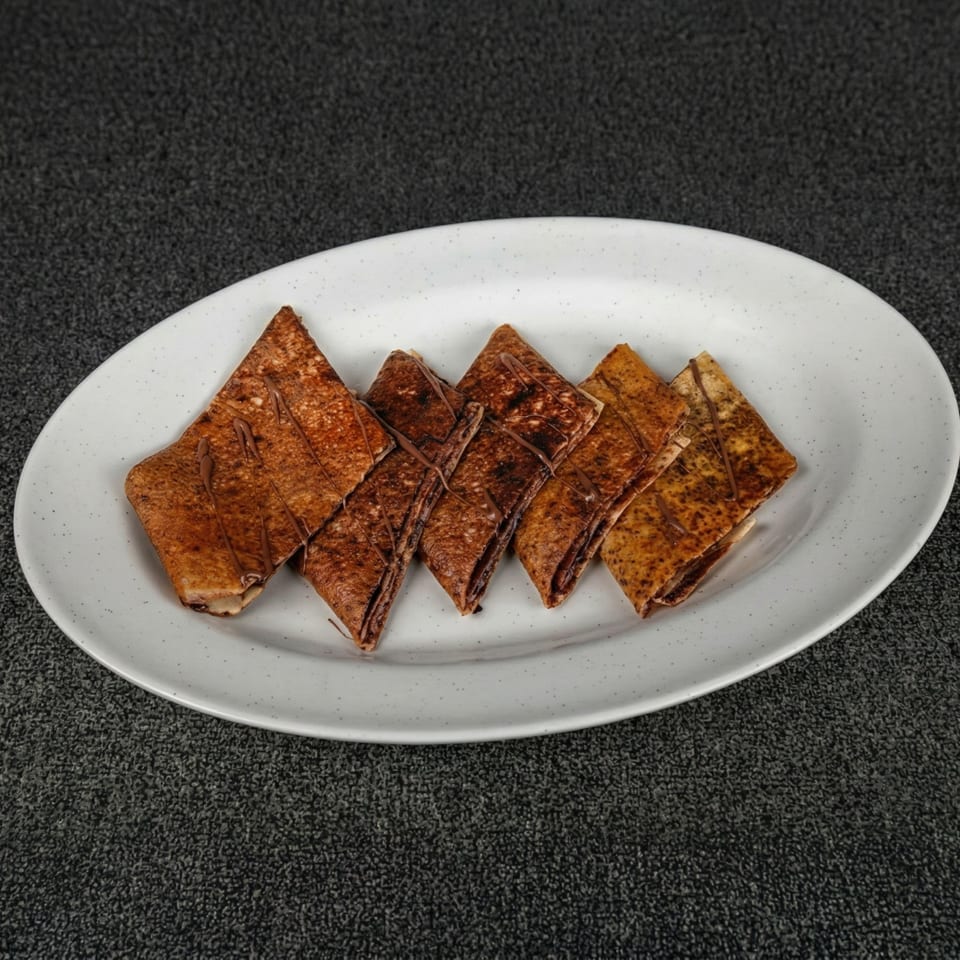 Five chocolate-drizzled crepes, folded into triangles, arranged on a white oval plate.